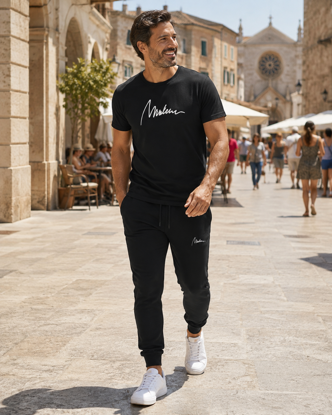 Hombre con jogger negro Marlene Black Motion y camiseta de firma blanca en calle histórica