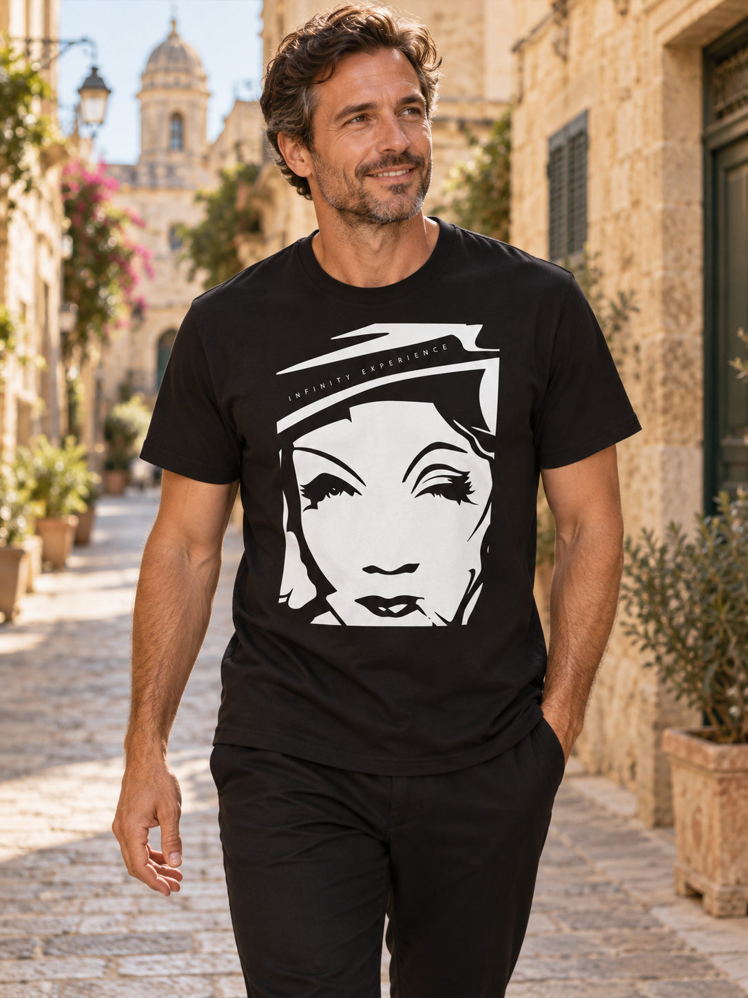 Hombre con camiseta negra White Icon de Marlene & Go y retrato blanco en una calle mediterránea; ambientación editorial generada.