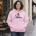 Rose Berlin: sudadera rosa claro con diseño original Marlene, llevada junto a una cafetería.